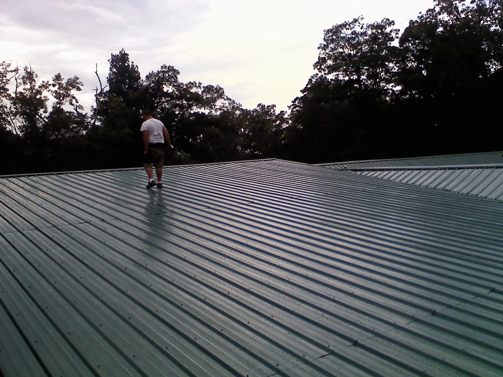 Roofer walking a wide expanse of new green metal roofing in Glendale