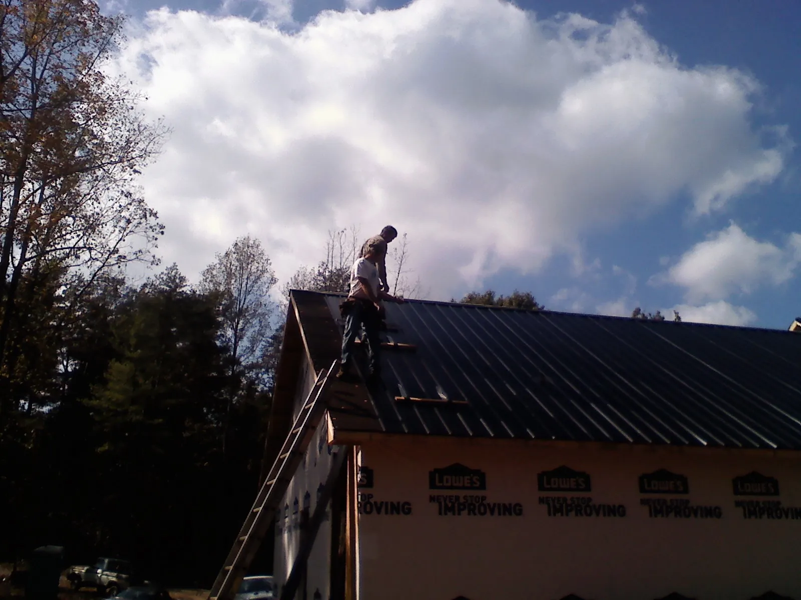 Roofer fastening dark metal panels high against a cloudy sky, from a Roof Inspection job in Glendale